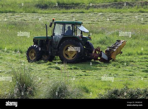 Green And Yellow John Deere Tractor Mowing Long Grass On A Sunny