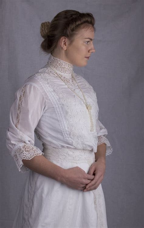 Edwardian Woman In White Blouse And Skirt Standing Against A Studio