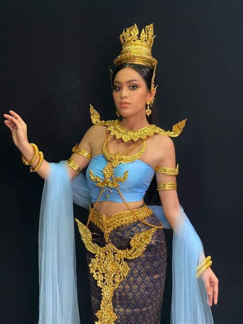 A Woman In A Blue And Gold Costume Standing Next To A Black Wall With Her Hands On Her Hips