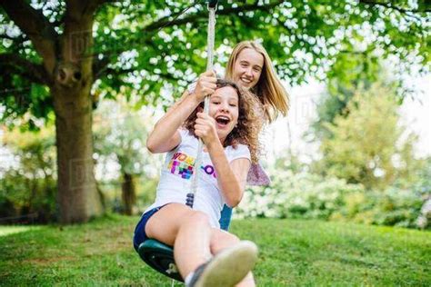 Two Tween Girls Swinging On Garden Rope Swing Stock Photo Dissolve