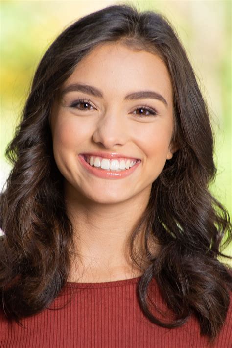 A Woman With Long Dark Hair Smiles At The Camera While Wearing A Red