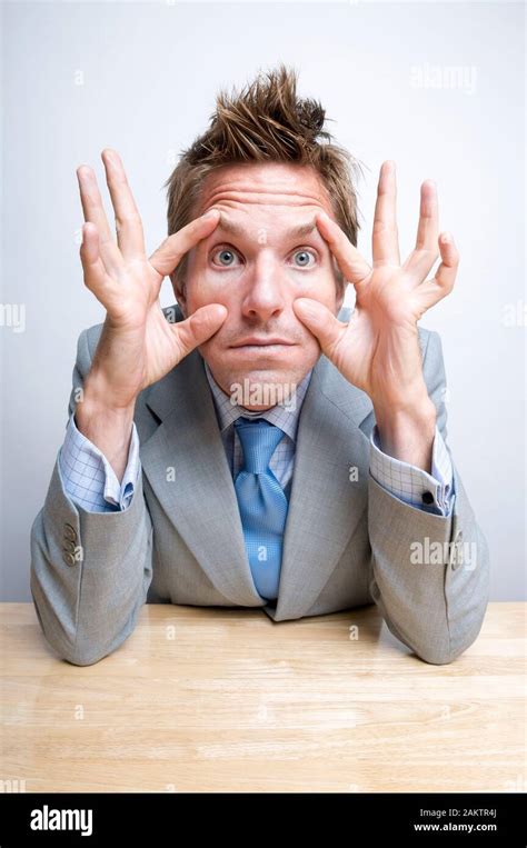 Tired Businessman Sitting At His Desk Holding Eyes Open With His