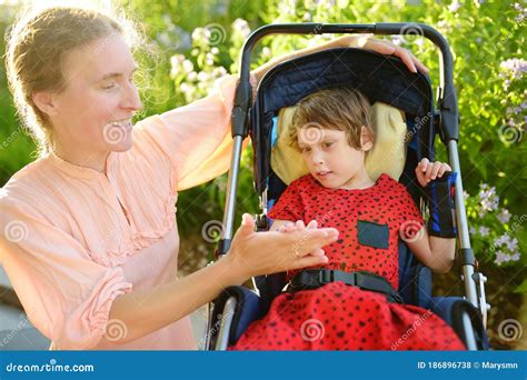 Woman With Disabled Girl In A Wheelchair Walking In The Summer Park