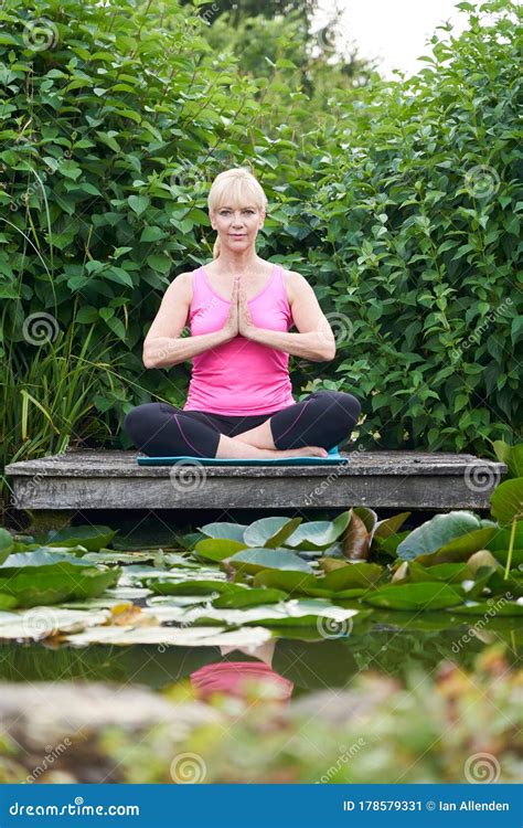 Portrait Of Mature Woman In Yoga Position On Wooden Jetty By Lake Meditating Royalty Free Stock