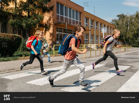 A Group Of Laughing Classmates Rushing Out Of School Crossing Road