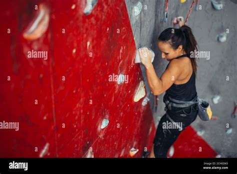 Adult Female Rock Climber On Red Vertical Flat Wall With Poor Relief