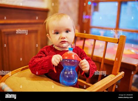 Little Baby Girl Sitting In High Chair At Home Or At Restaurant And