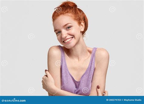 tender shy woman with positive smile embraces herself tilts head has foxy hair combed in bun