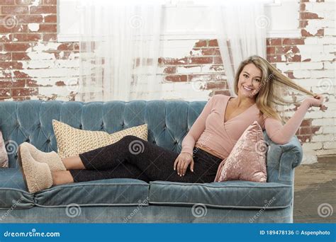 Gorgeous Blonde Woman Relaxes On Couch In Living Room Stock Photo