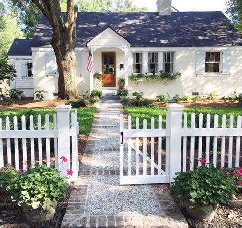 A White Picket Fence In Front Of A House With Flowers On The Ground And