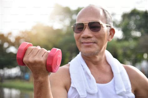 happy asian senior man wear sunglasses exercising with lifting dumbbell at park outdoor photo