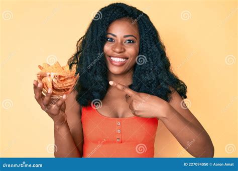 Beautiful African Woman Holding Nachos Potato Chips Smiling Happy Pointing With Hand And Finger