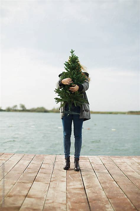 Young Woman Standing On Dock And Holding A Christmas Tree By Jovana