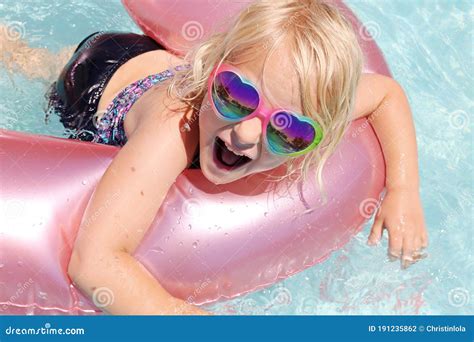 szczęśliwa mała letnia dziewczynka unosząca się w różowej tratwie w basenie na podwórku zdjęcie