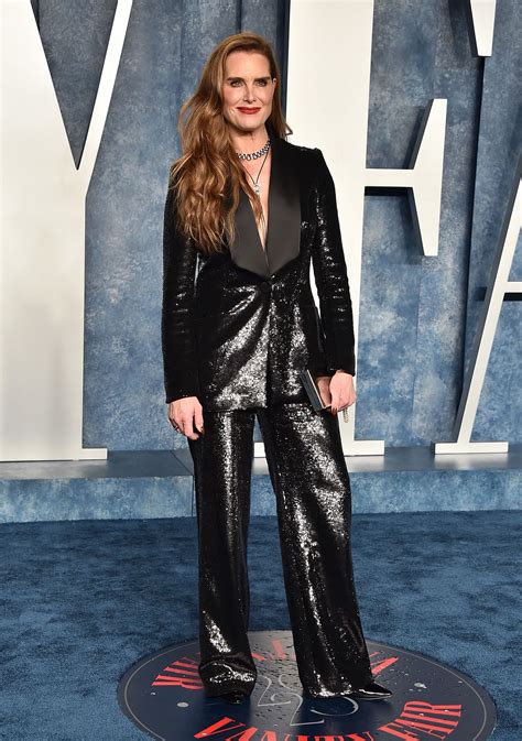 A Woman In A Black Suit Standing On A Blue Carpet With Her Hands In Her