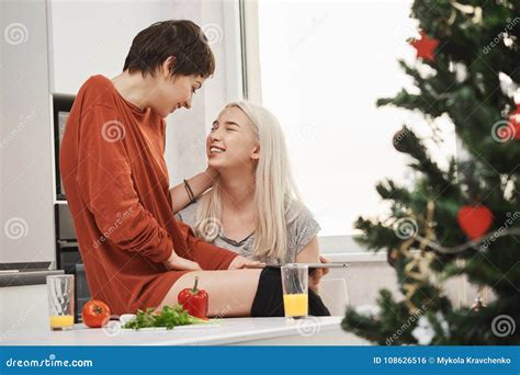 two cute girls sitting in kitchen while talking and laughing during breakfast near christmas