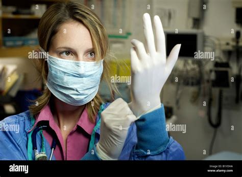Female Nurse In Scrubs With Face Mask Putting Gloves On Hospital Setting Background Stock Photo