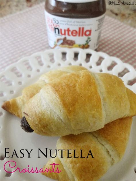 Two Croissants On A White Plate With Nutella Spread In The Background