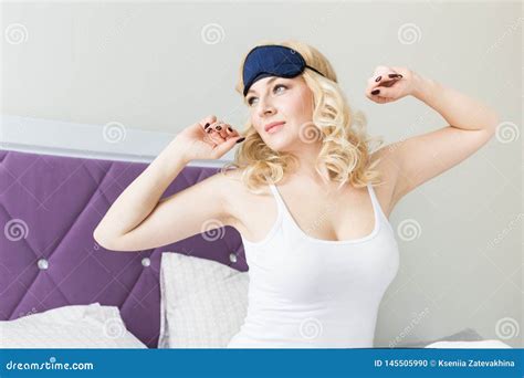 A Beautiful Blonde Woman Wakes Up And Snares A Mask For Sleeping In Her Bed In The Morning Stock