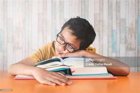 Young Asian Male Student Fall Asleep On A Stack Of Books While Studying