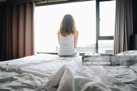 Portrait Of Depressed Woman Sitting Alone On Bed Looking To Outside The