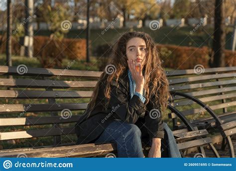 Sad Brooding Girl With Long Brown Hair Sits On Bench In Autumn Park And