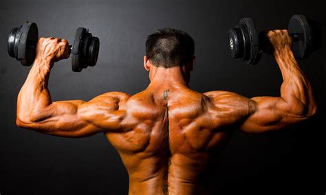 Rear View Of Bodybuilder Training With Dumbbells On Black Backgr