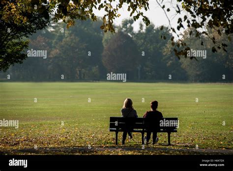 Two People Sit On A Bench In A London Park Stock Photo Alamy