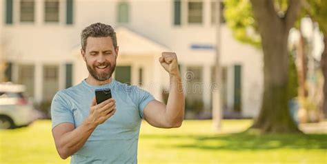 Happy Mature Man Standing Outdoor At House Reading Message On Smartphone Real Estate Stock