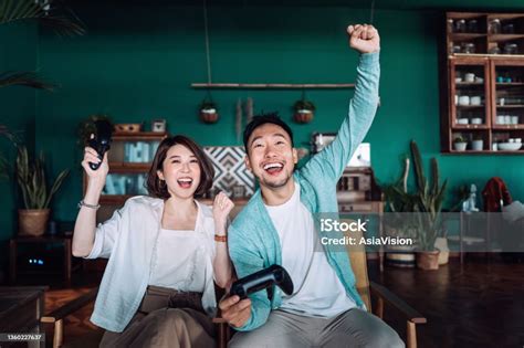 Happy Young Asian Couple Sitting On The Sofa In The Living Room Shouting In Excitement While