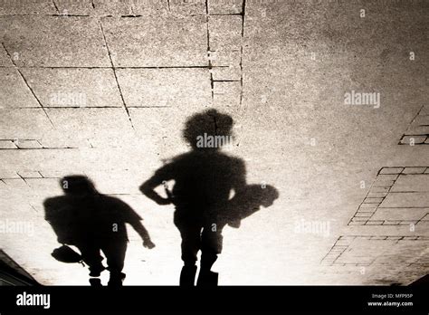 Shadow Silhouette Of A Boy And A Man Walking Od The City Sidewalk In