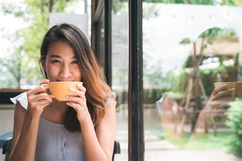 Free Photo Cheerful Asian Young Woman Drinking Warm Coffee Or Tea Enjoying It While Sitting In
