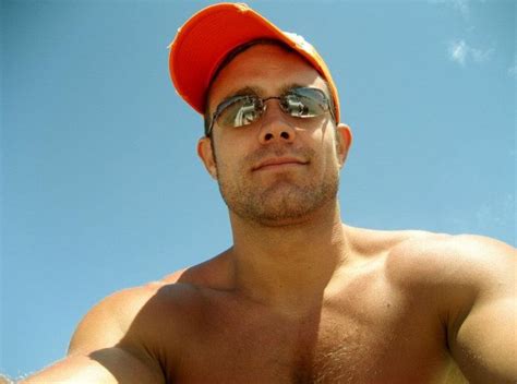 A Man With No Shirt Wearing Sunglasses And An Orange Baseball Cap Is