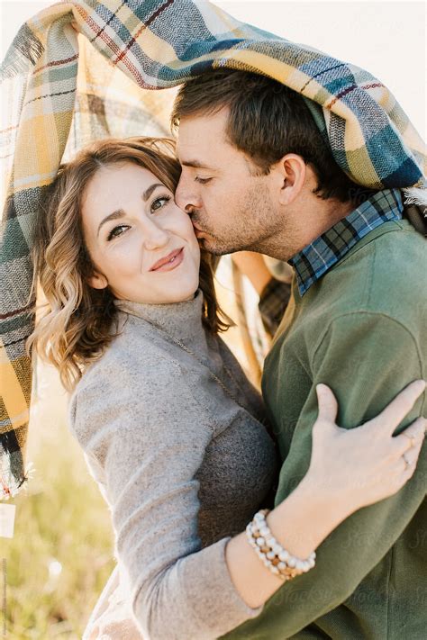A Husband Kissing His Wife On The Cheek Under A Plaid Blanket