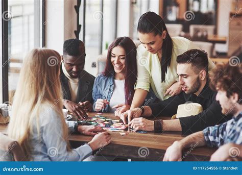 Group Of Creative Friends Sitting At Wooden Table People Having Fun While Playing Board Game