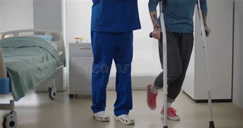 Doctor Helping Female Patient In Crutches At Hospital Ward Stock Photo