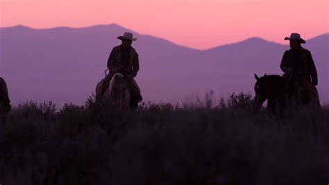 Slow Motion Shot Of Cowboys Riding Towards The Camera With Pink Sky In