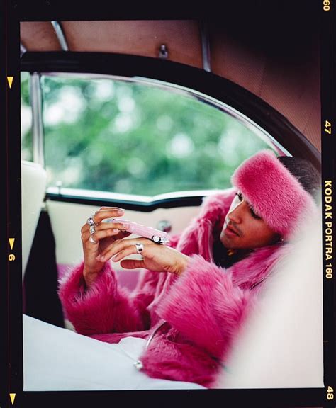 a woman in a pink fur coat sitting in a car looking at her cell phone