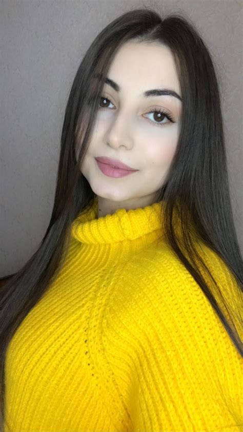 a woman with long black hair wearing a yellow turtle neck sweater and posing for the camera