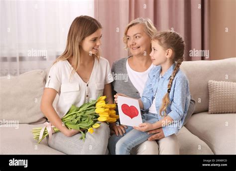 Niña Felicitando A Su Madre Y Abuelita Con Flores Y Postal En Casa