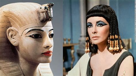 An Egyptian Woman Wearing Gold Earrings Next To A Statue Of The Queen