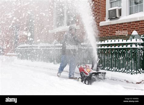 A Man Clears The Sidewalk With A Snow Blower During Winter Storm