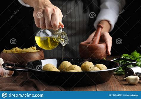 Woman Pouring Oil Onto Frying Pan With Raw Falafel Balls At Wooden