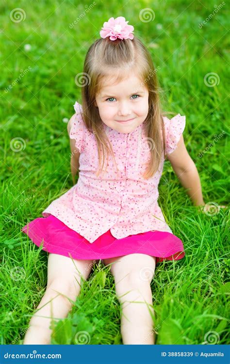 Маленькая девочка при длинные светлые волосы сидя на траве Стоковое Изображение изображение