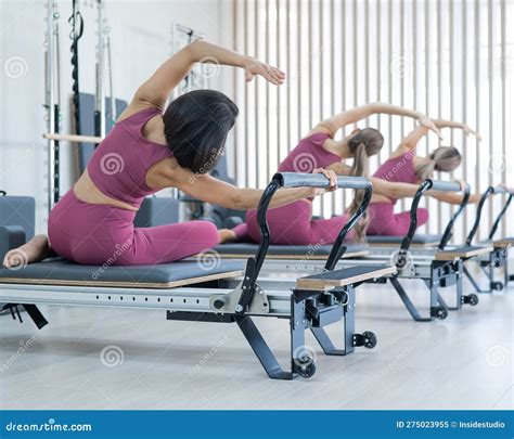 Three Asian Women In Pink Sportswear Doing Side Bends On A Reformer Machine Pilates Classes