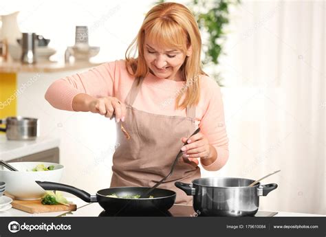 Beautiful Mature Woman Cooking In Kitchen Stock Photo By ©belchonock