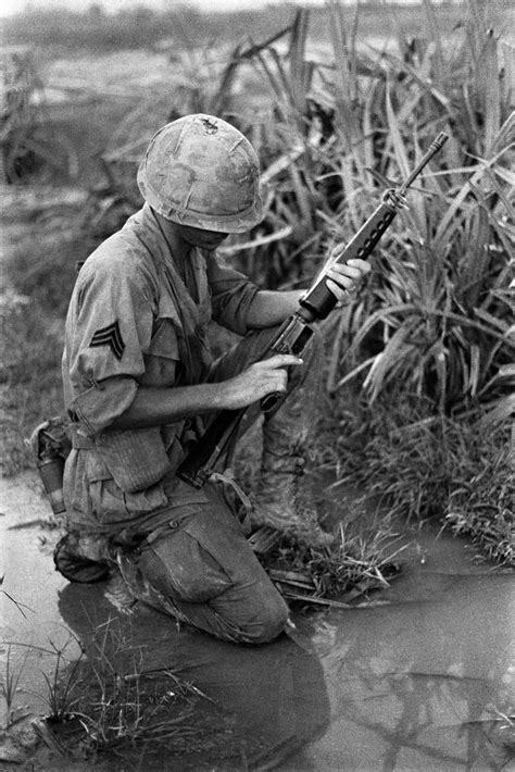 A Us Army Sergeant Kneels On Wet Ground And Checks His M16 Rifle South Vietnam Date Unknown