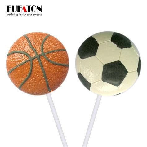 Top view of heart shaped chocolate candy on round board with cutlery isolated on black. Sport basketball and football shaped candy lollipops