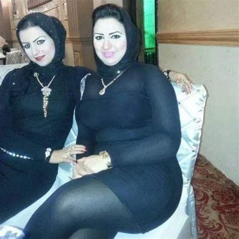 Two Women Dressed In Black Sitting On A White Couch With Their Arms Around Each Other