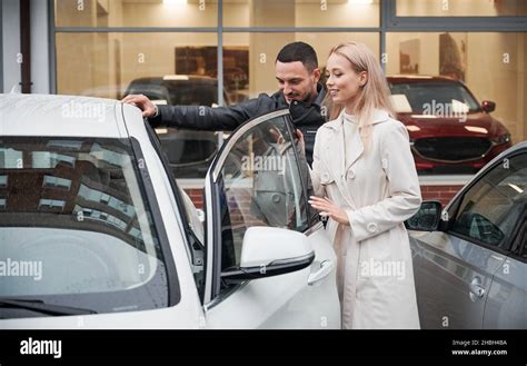Young Woman And Man Opening The Front Door Of New Auto And Examining Car Interior While Visiting